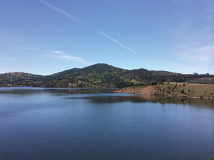 A still lake of water surrounded by tree-covered hills.