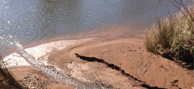 A small inlet to a lake edge is full of fine red-brown dirt.