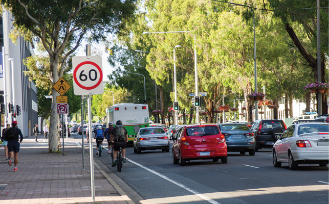 A busy three-lane road with cars, buses and cyclists